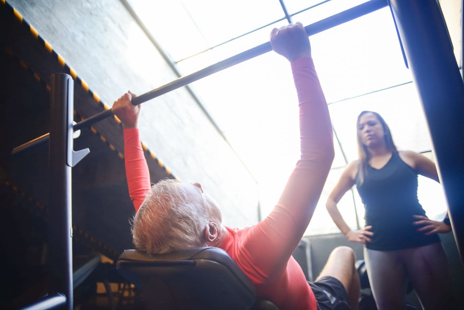 Hombre mayor entrenando fuerza en un gimnasio con una entrenadora