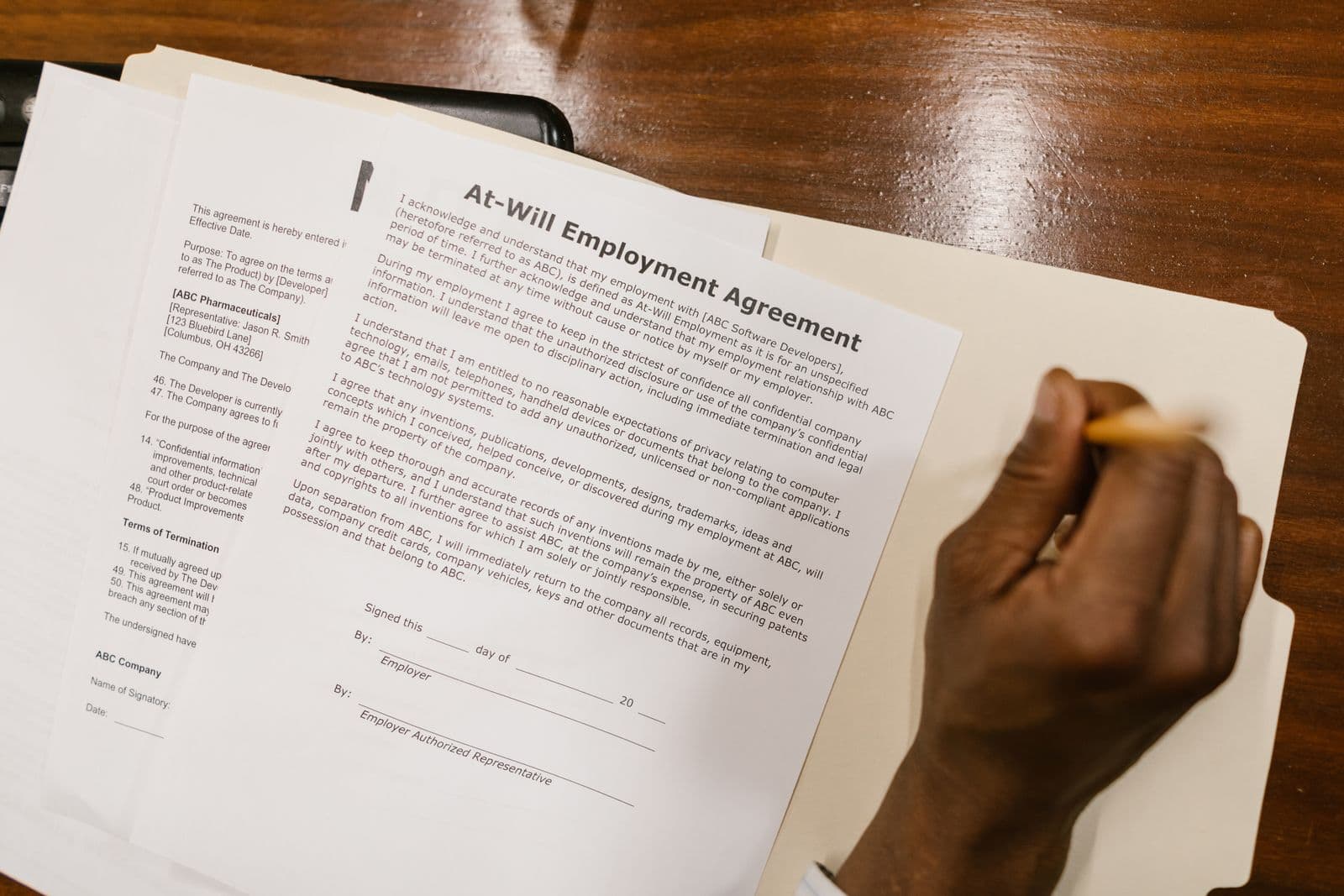 Mano firmando un contrato de trabajo sobre un escritorio de madera